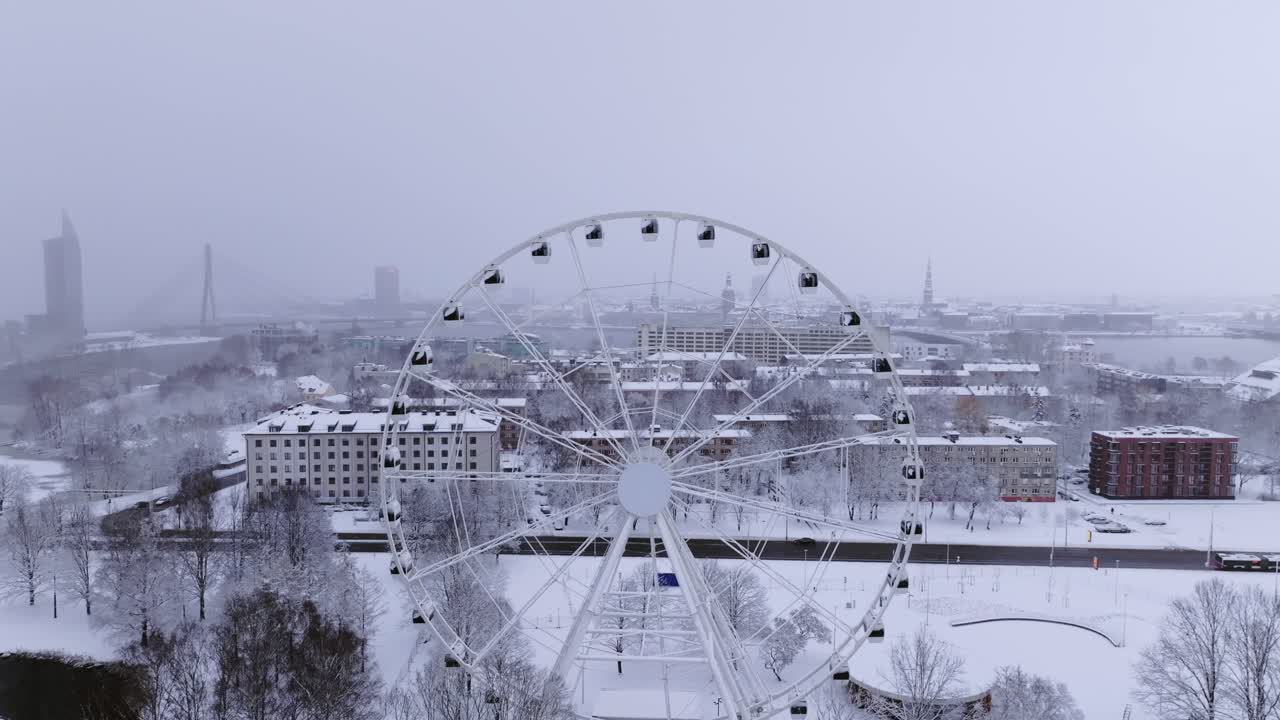 Drone rotates left above snowy Riga skyline showing Ferris wheel in winter park