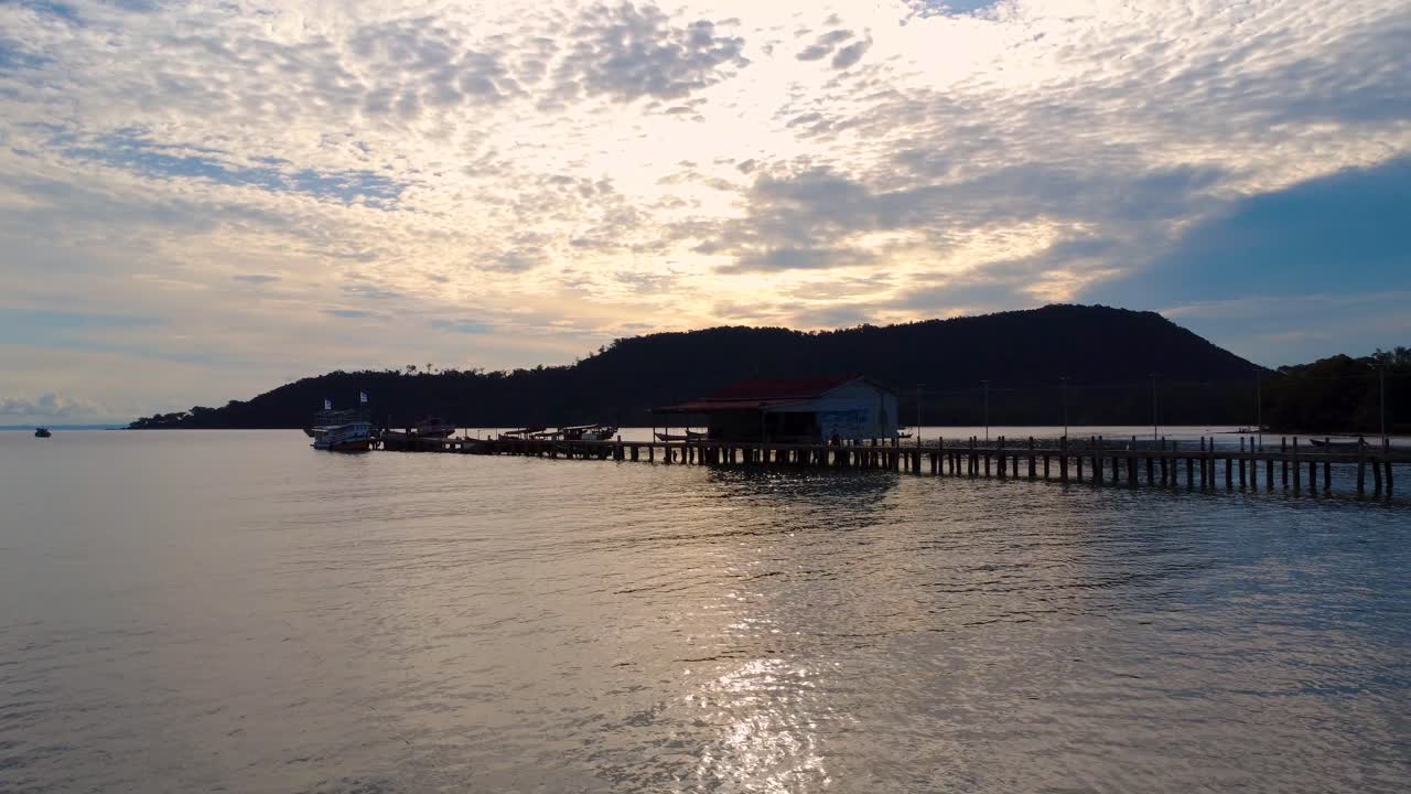calm evening scene with a small boat resting near a long wooden pier at sunset. Filmed at Mpai Bay on Koh Rong Samloem island near Sihanoukville City in Cambodia