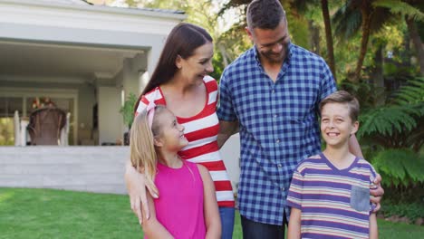 retrato de padres caucásicos felices, hijo e hija de pie en el jardín juntos sonriendo