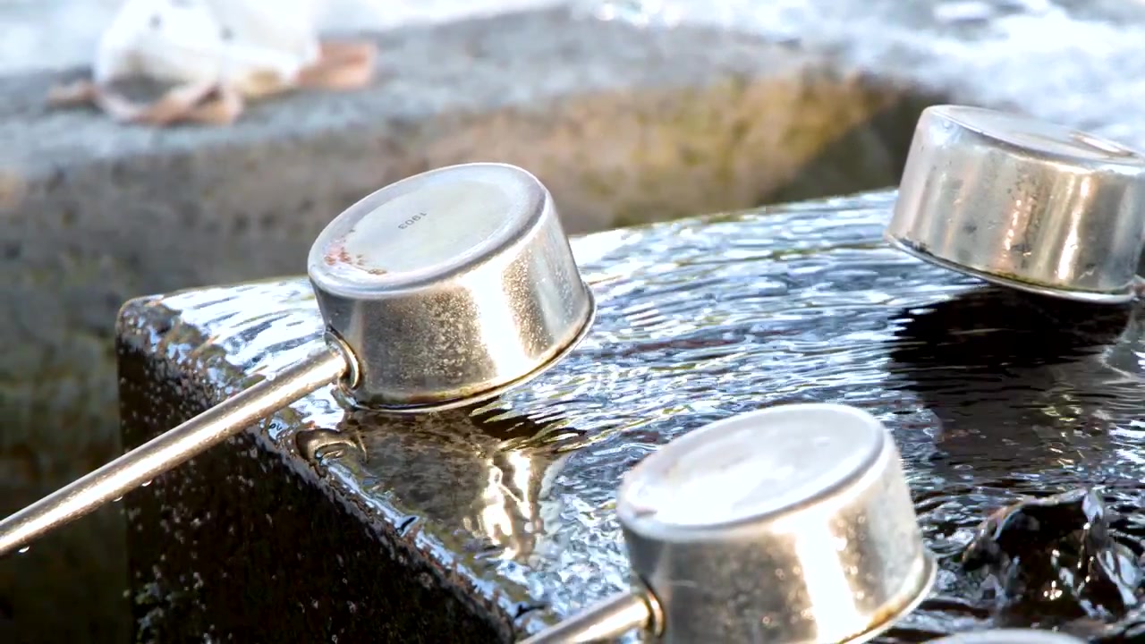 Primo piano di mestoli di metallo appoggiati su una vasca di pietra con acqua che scorre in Giappone.