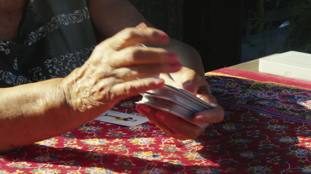 Mani anziane che mescolano un mazzo di carte da gioco a un tavolo da giardino estivo