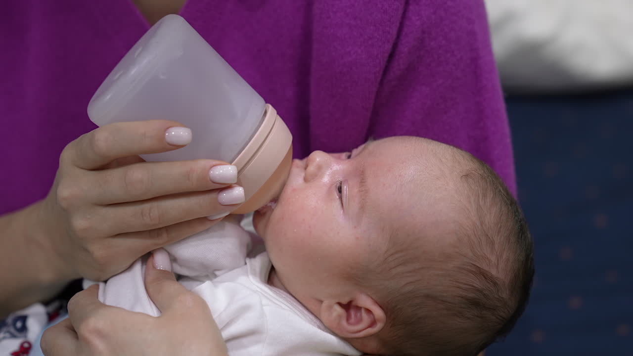 Sweet little baby eating milk from a bottle in mommy's hands. Baby finishing the bottle and lets go the bottle pacifier. Suckling baby close up.