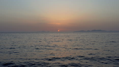 Aerial:-Drone-footage-flying-low-over-sea-towards-horizon-during-sunset