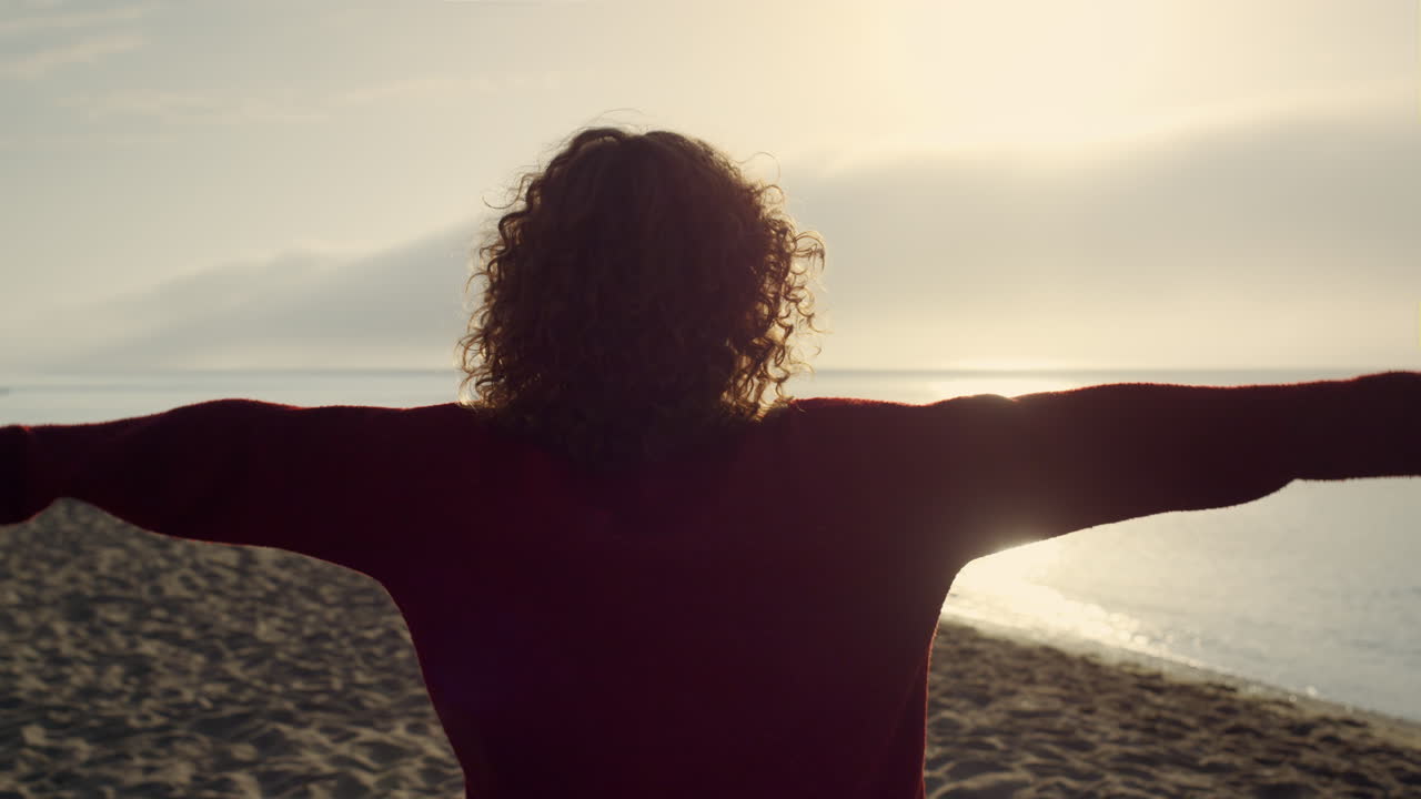 Casual woman raising hands on beach. Romantic girl feeling freedom at sea