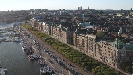 Verkehr-Und-Fußgänger-Auf-Strandvägen-Und-Strandkajen,-Stockholm-An-Einem-Sonnigen-Abend-Mit-Sichtbaren-Alten-Wohnhäusern-Und-Skyline