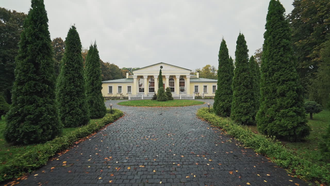 Wet pavement which leads to the big light building in the park. Beautiful alley with green trees and a nice architecture in peaceful landscape garden in autumn.