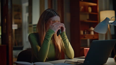 tired woman calling smartphone working at laptop in night apartment close up.