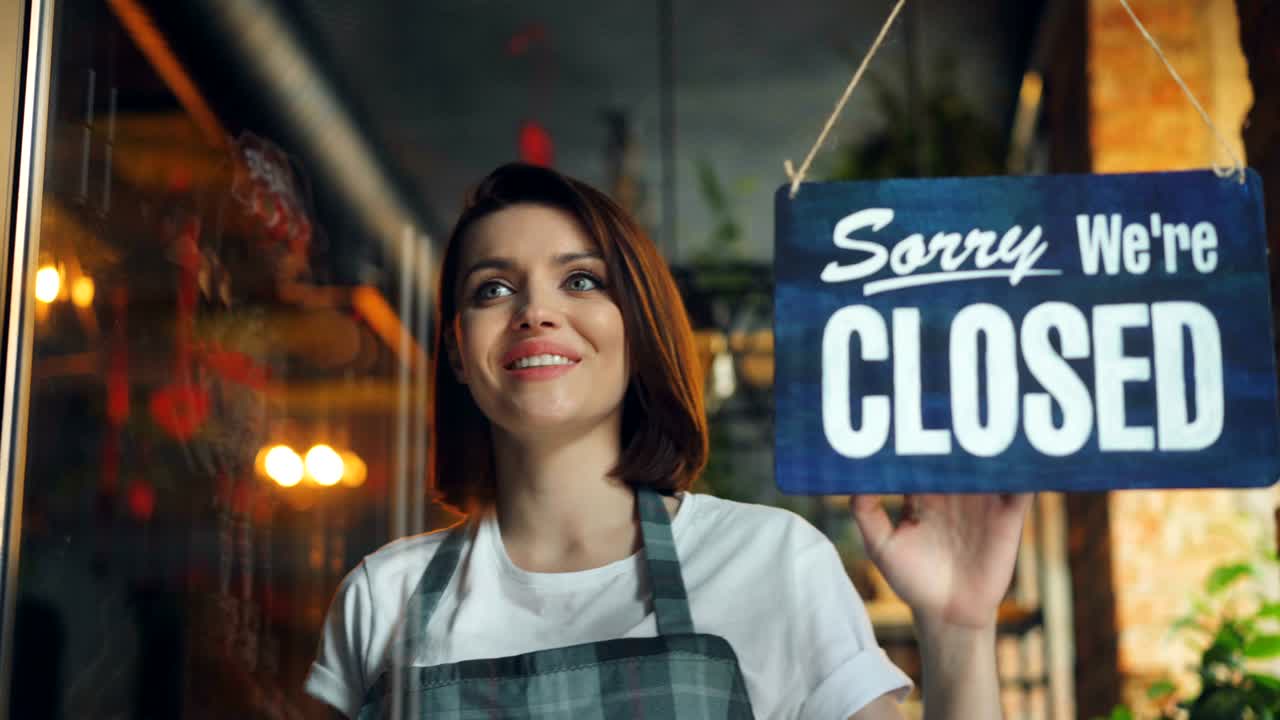 Beautiful waitress closing coffee shop in evening hanging closed sign on door
