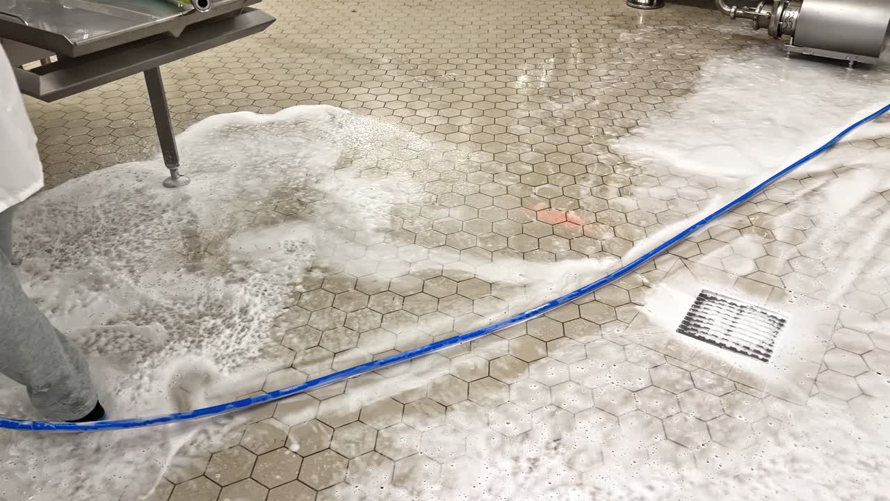 Person cleaning industrial floor with hose in food processing area