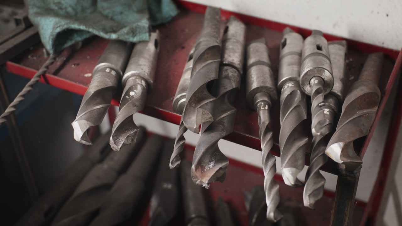 Close-up of heavy-duty steel twist drills on a red shelf in a workshop