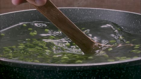 Cocinar-Los-Guisantes-En-Una-Olla,-Agitando-El-Agua-Con-Una-Espátula-De-Madera