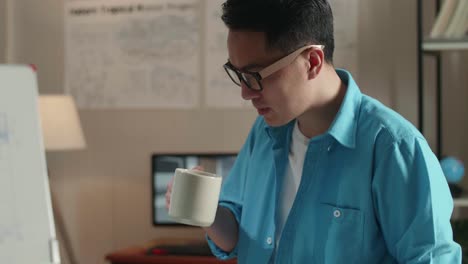 close up of asian man engineer sitting on the table and drinking coffee while using a laptop to work at the office