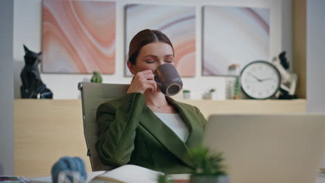 smiling boss relaxing latte cup sitting workplace closeup. woman drinking coffee