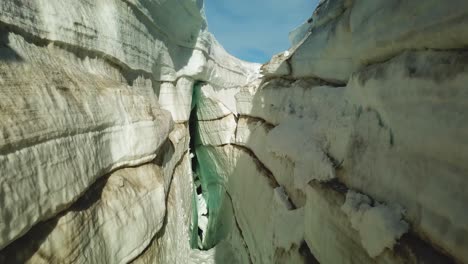 Aerial-rising-view-inside-a-ice-crevasse,-cracked-on-the-ice-surface-of-an-icelandic-glacier,-on-a-sunny-day