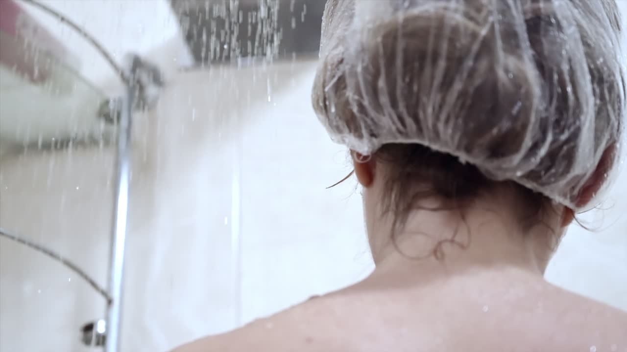 Close up of a woman showering with a shower cap on her head
