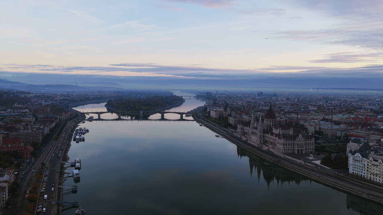 A tranquil aerial view of Budapest at dawn, the Danube River splitting Buda and Pest, bridges arching gracefully under a pastel sky