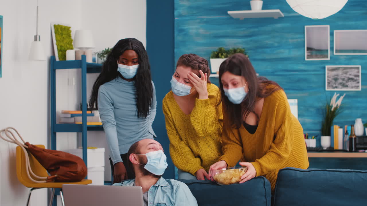 Mixed race friends with face masks looking in laptop at funny clip