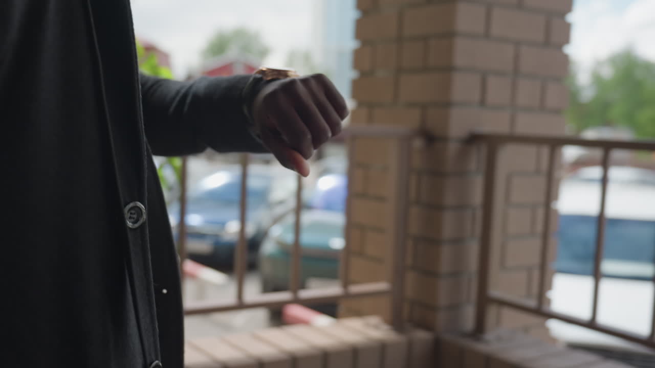 Close view highlights man in thick suit jacket, crisp button row and metal wristwatch, sleeve edge grazing polished case, tailored fabric texture and clean lines conveying business elegance mood