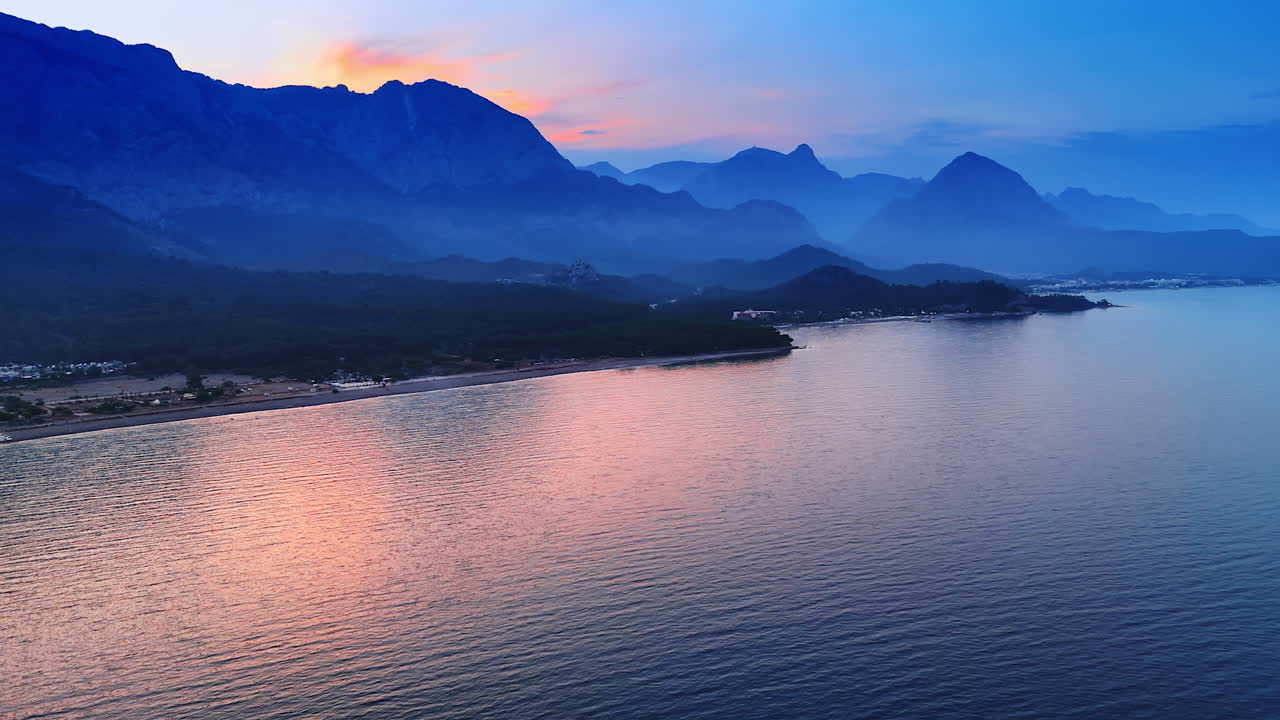 Beautiful silhouettes of the mountains covered with haze. Dusk time at the rocky shore of the sea or ocean. Aerial view