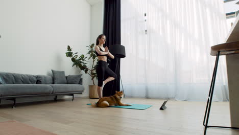 a young female does yoga at home with her dog next to her