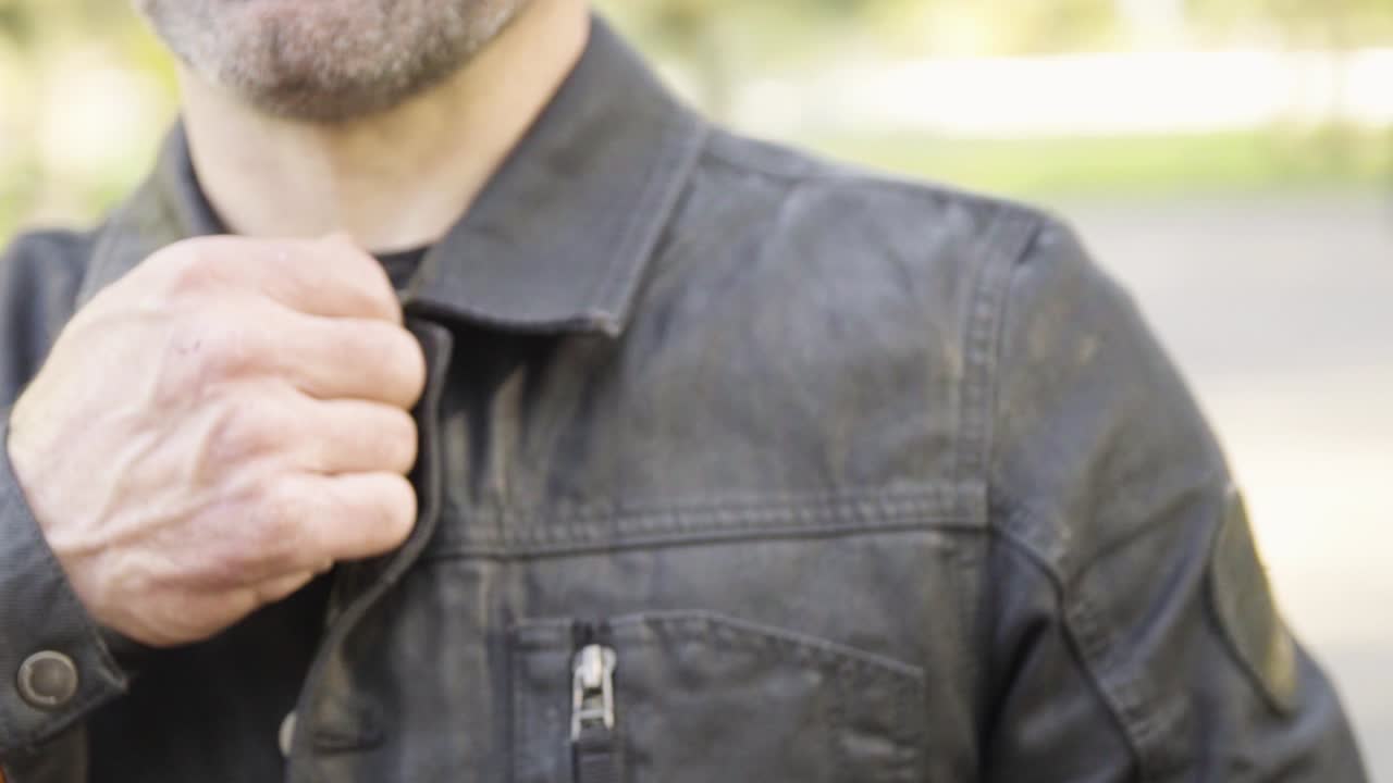 Man dressed up in professional motorcycling clothes fastens the leather jacket with a zipper in forest during golden hour in slow motion