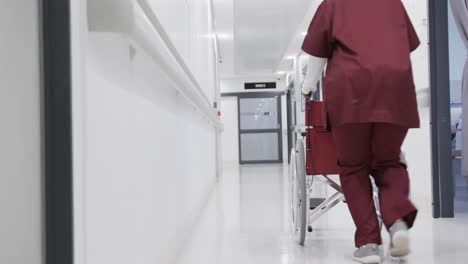 african american female doctor running with wheelchair in hospital corridor, slow motion