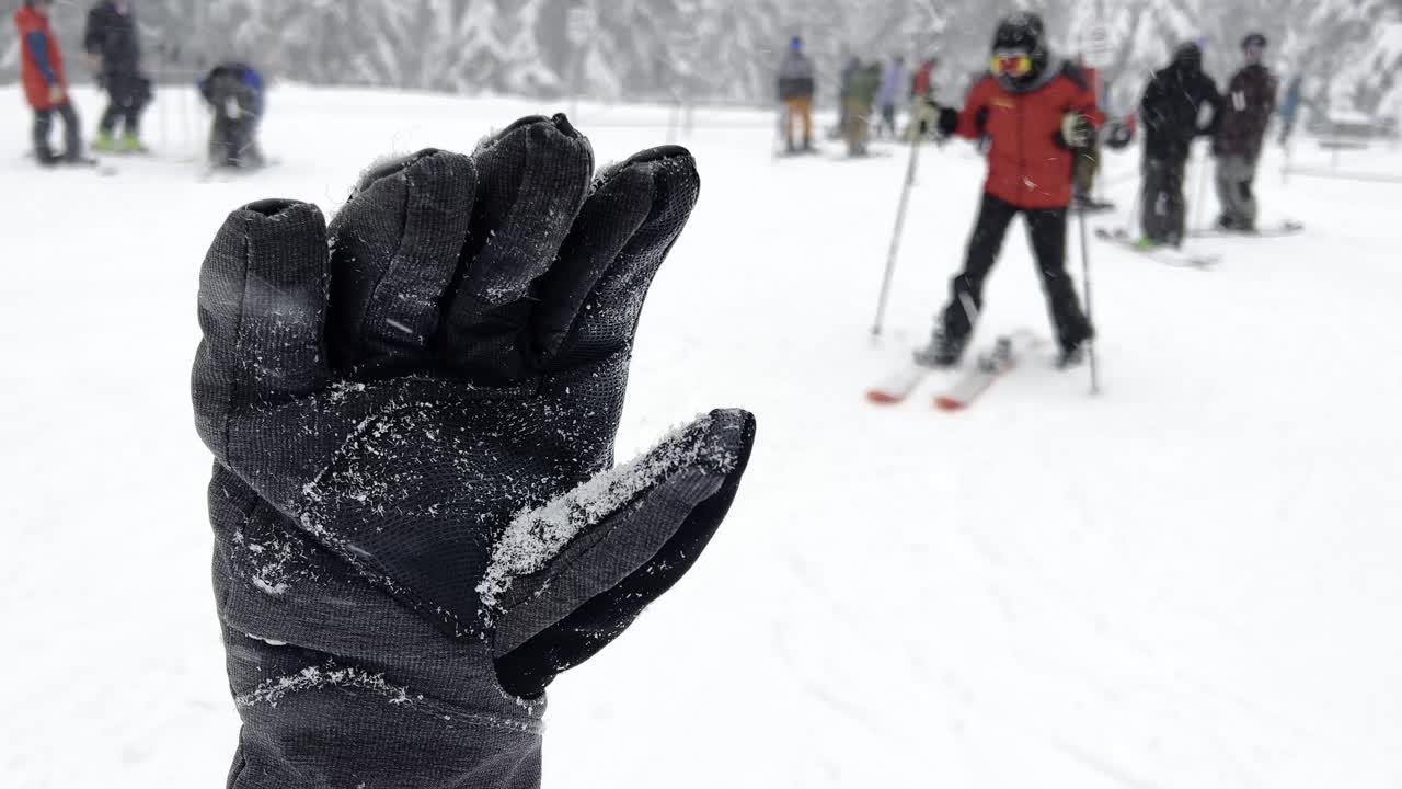 guante de invierno negro cubierto de nieve durante una nevada con muchos esquiadores en el fondo