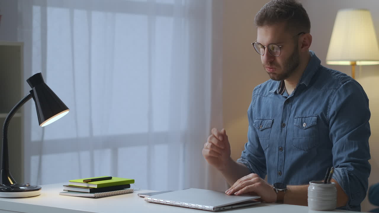 hombre cansado está apagando la computadora portátil y la lámpara de mesa después de trabajar demasiado en casa trabajo remoto por la noche frotando la cara y los ojos quitando las gafas