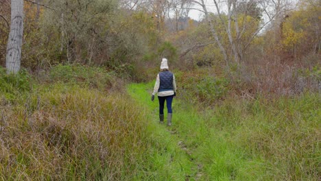 woman in stocking cap walking through lush, damp woods on a cloudy, january day