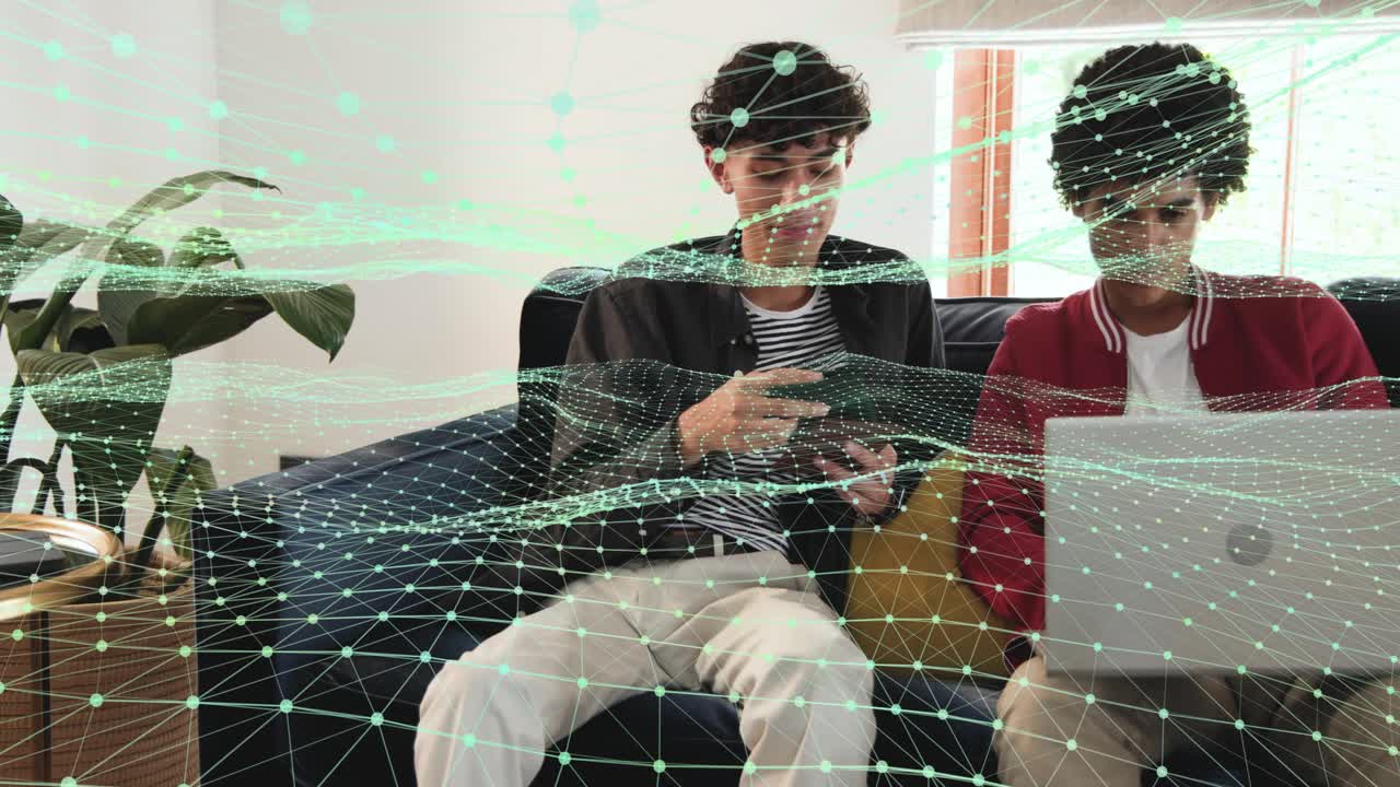 Left peer tapping tablet, guiding right peer typing silver laptop with grid overlay for tech review