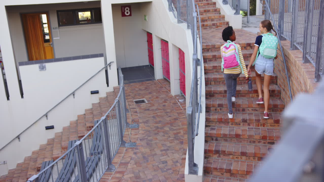 Walking up stairs, two girls with backpacks heading to classroom in school, copy space