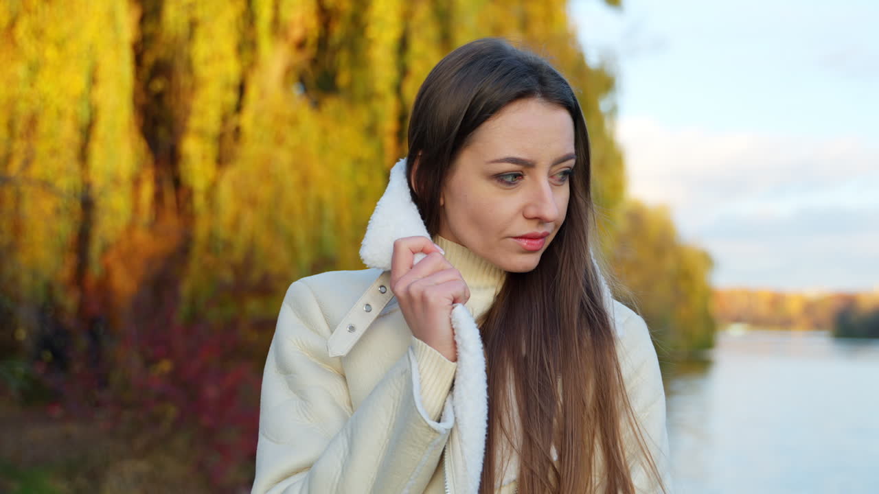 Woman in a white coat by the river in autumn