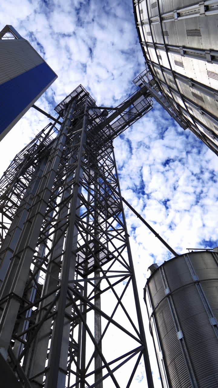 Metal construction on a modern industrial plant. Large grain elevators on beautiful sky background. View from below. Vertical video