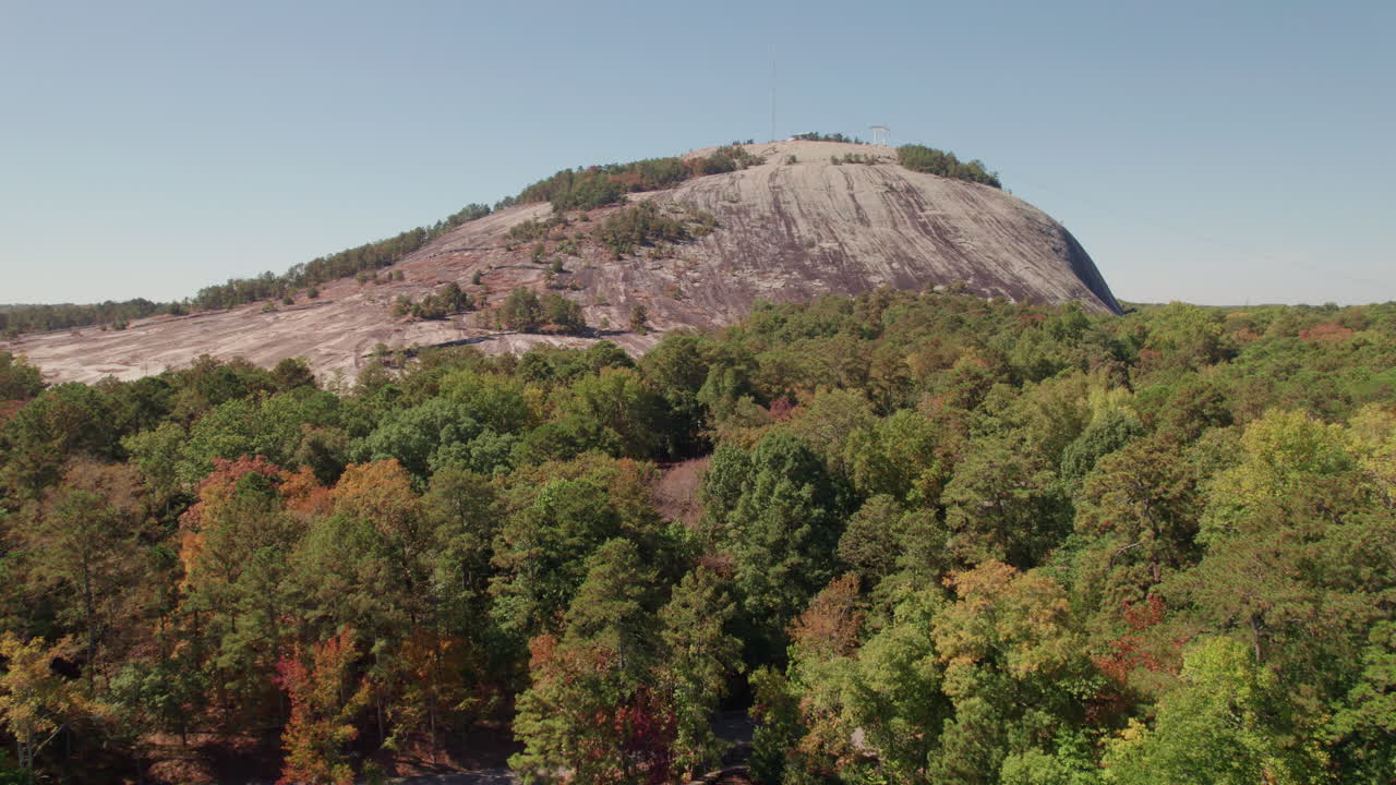 A cinematic aerial tracking over the lush tree canopy and river approaching Stone Mountain in the popular state park for hiking, tourism, kayaking, cycling, and outdoor recreation in Georgia.