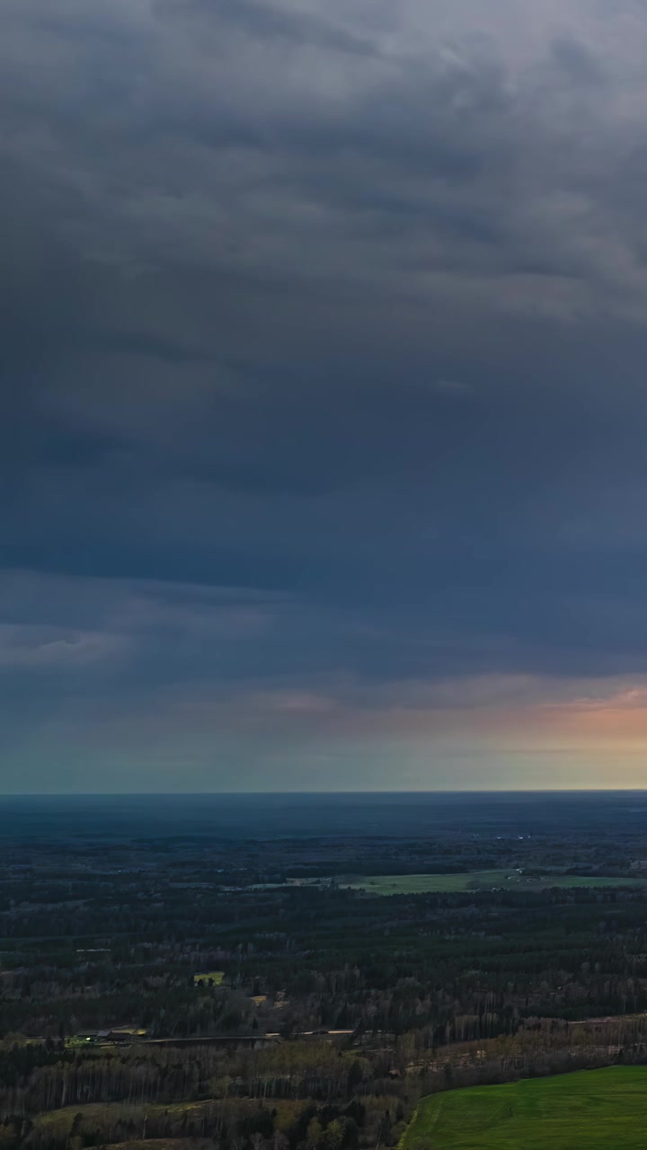 Aerial timelapse of dramatic rain clouds over the rural countryside at sunset with sunlight illuminating the horizon