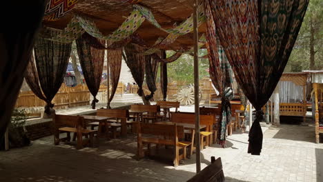 Leere-Terrasse-Des-Restaurants-Mit-Orientalischem-Vorhang-Und-Sonnenschirm-An-Heißen-Sonnigen-Tagen,-Chiwa,-Usbekistan