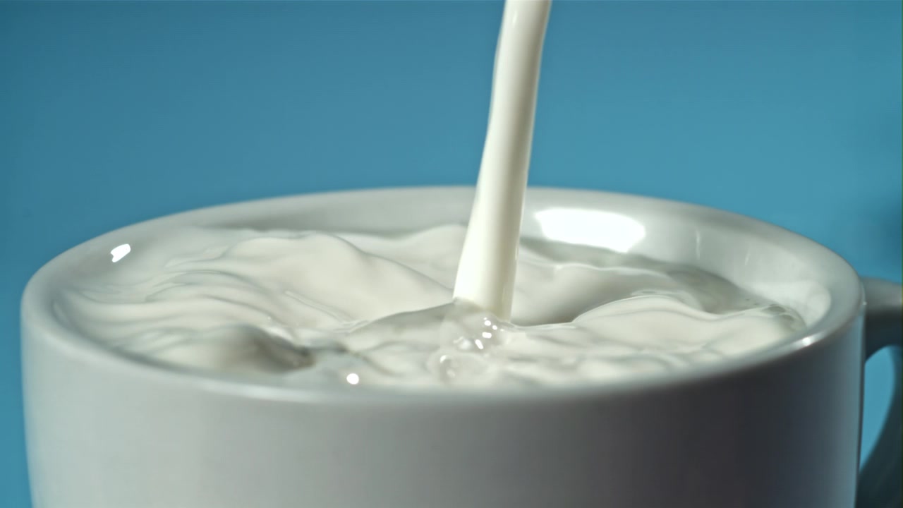 青い背景で白いカップに牛乳を注ぐスローモーション。