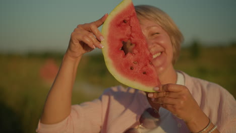 mujer sosteniendo una rodaja de sandía con un recorte en forma de estrella, sonriendo e inclinando su cabeza de un lado a otro lúdicamente, el fondo borroso verde mejora el verano