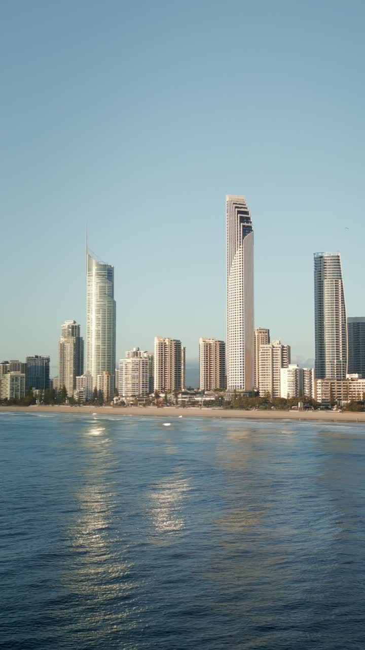Vertical drone of surfers on boards further out in ocean with Surfers Paradise skyline background, Gold Coast Queensland Australia. Surf culture perspective showcasing beach lifestyle and coastal