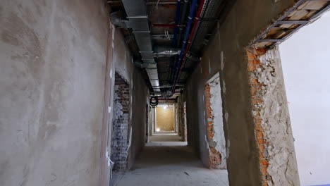 movement by the long corridor being under reconstruction. hall with grey unfinished walls and pipes on the ceiling.