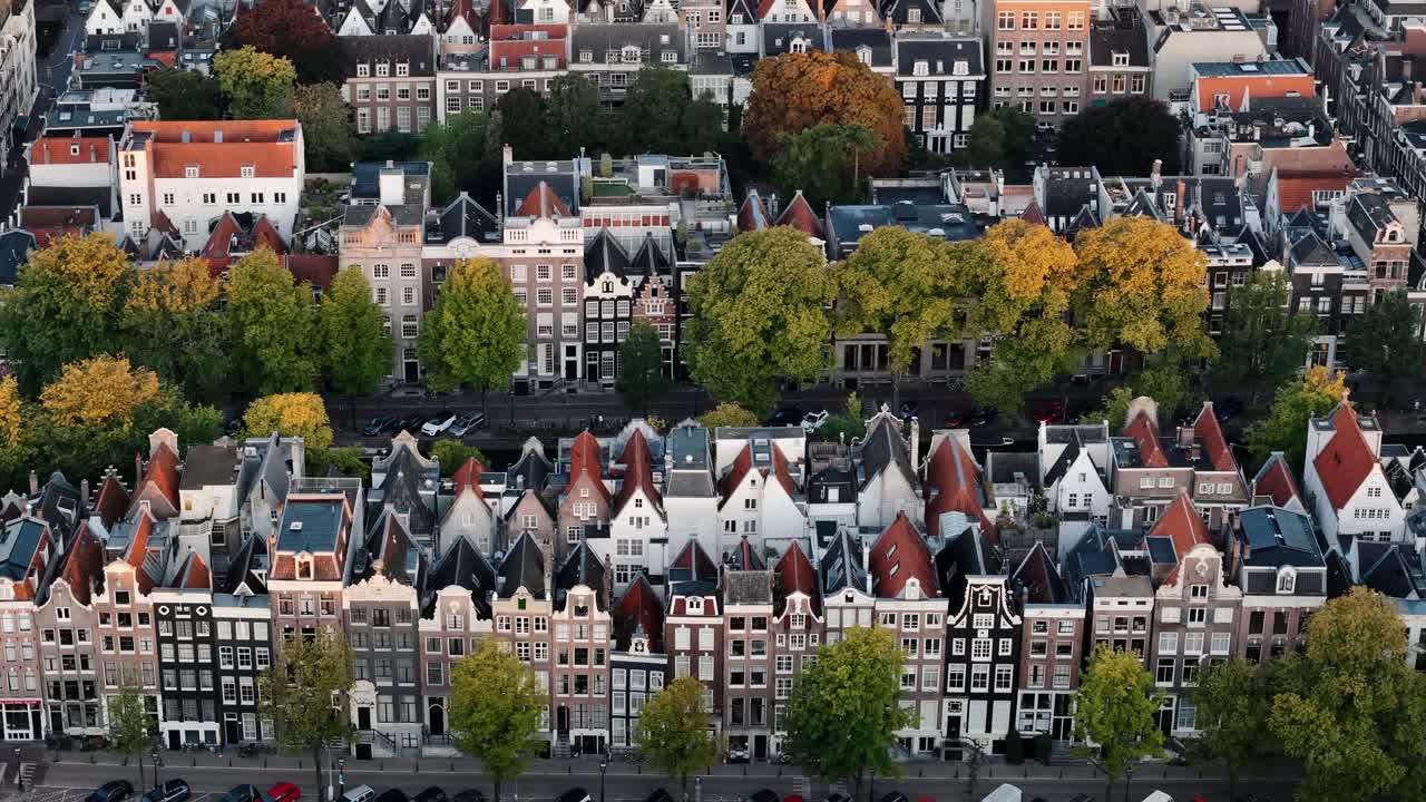 Descending drone pans up over rows of houses at sunrise in Amsterdam, establishing