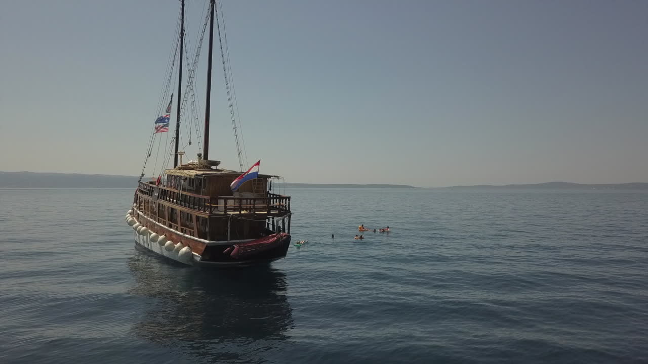 Orbiting aerial of live-aboard tour ship in Adriatic Sea flying flags
