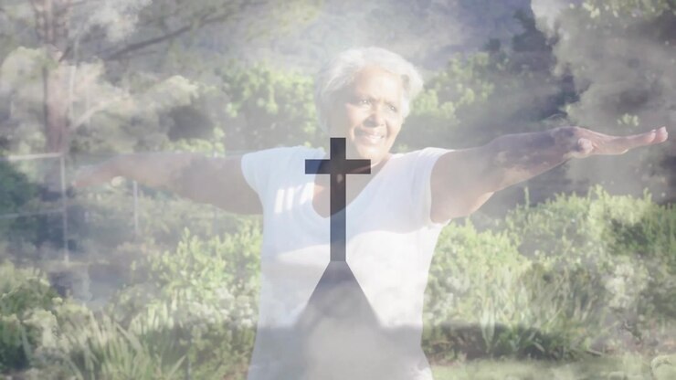 Senior woman raising arms while activating cross silhouette and clouds drifting over garden
