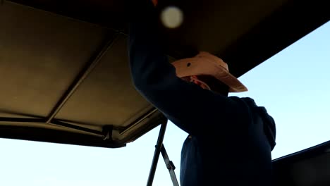 a young man with a safari hat traveling in a jeep, holding off the roof as going on a bumpy road offroad, looking for animals