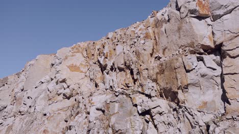 Acantilado-Escarpado-Con-Texturas-De-Roca-Detalladas-Bajo-Un-Cielo-Azul-Claro