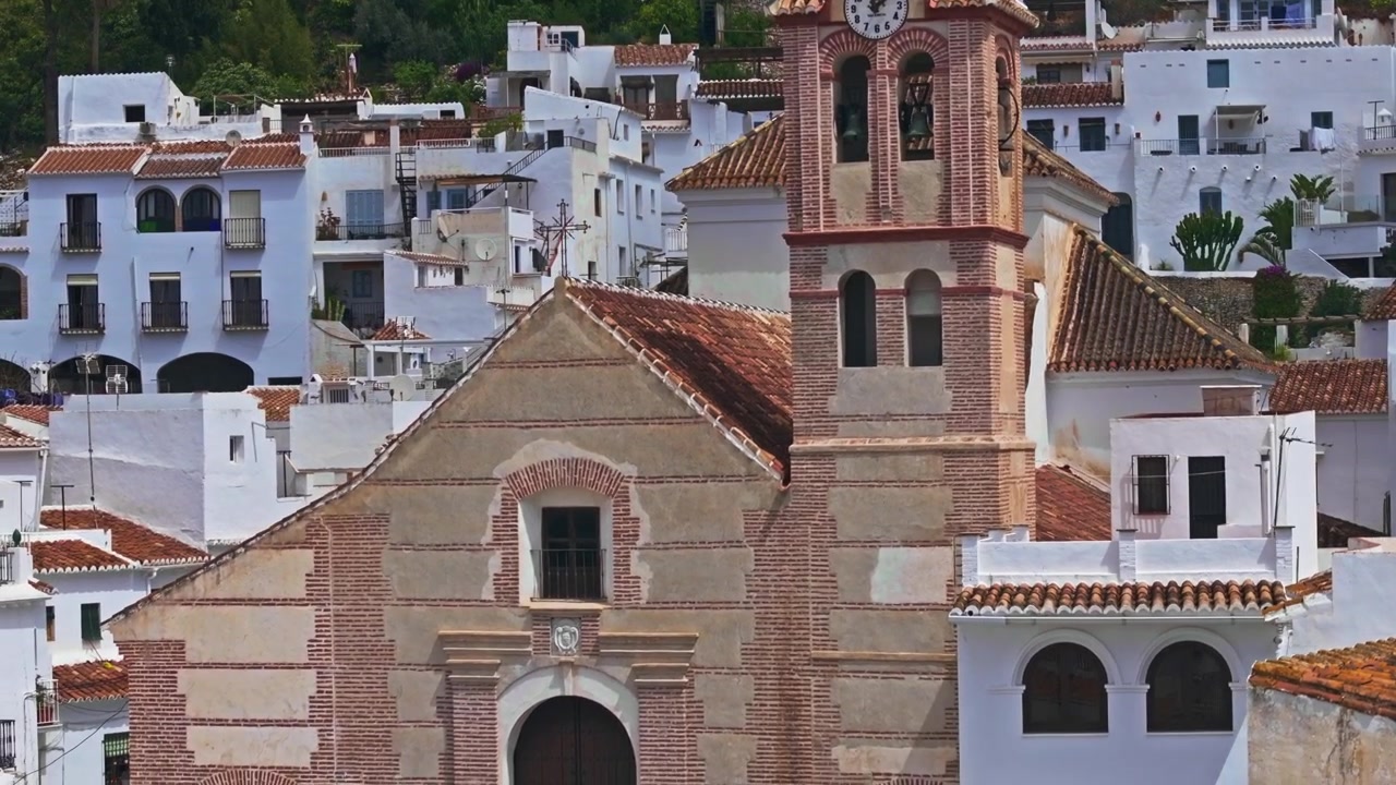 Filmato drone di Frigiliana, Andalusia, Spagna, con una vista zoom compressa di un campanile, case imbiancate a calce del villaggio e un tranquillo paesaggio collinare