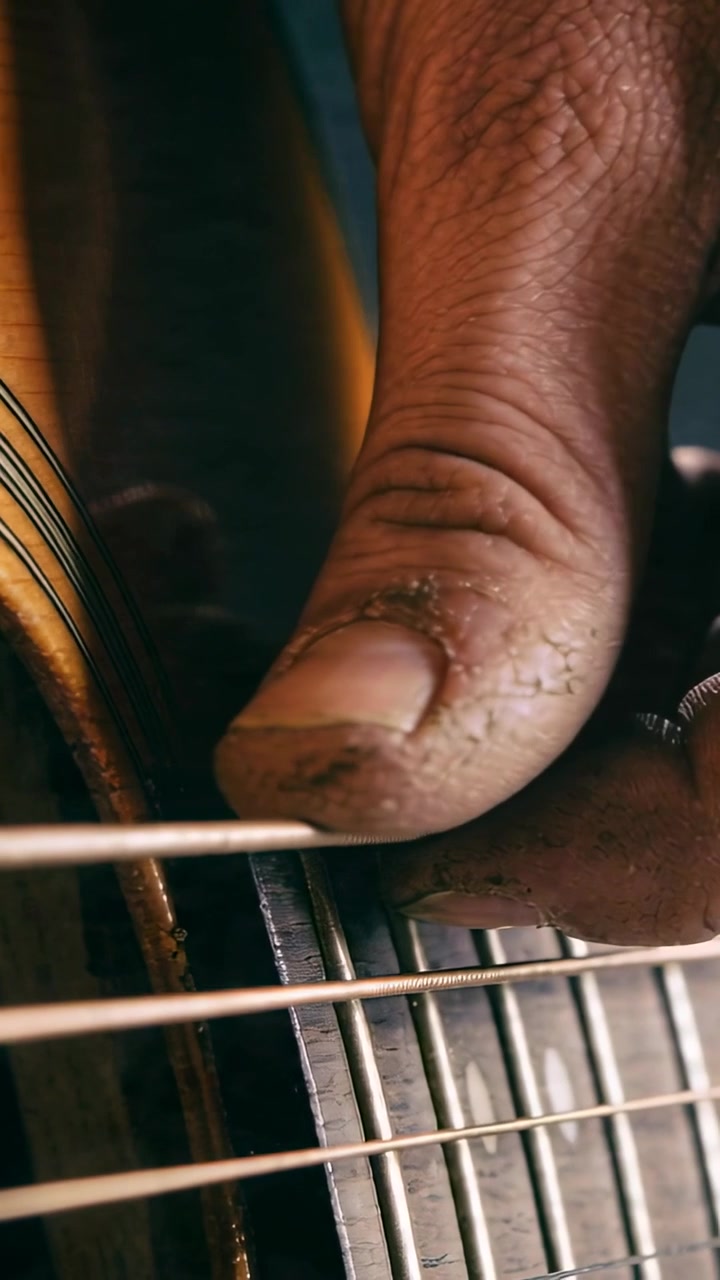 Video verticale: Il pollice destro di un musicista che pizzica e poi tira una corda di chitarra in una stanza, creando musica.