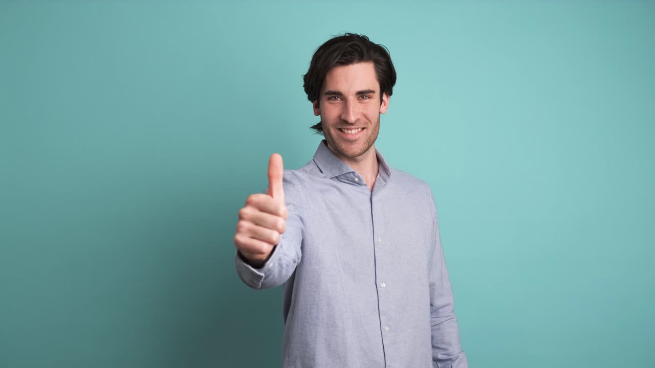 Happy man showing thumbs up in blue studio