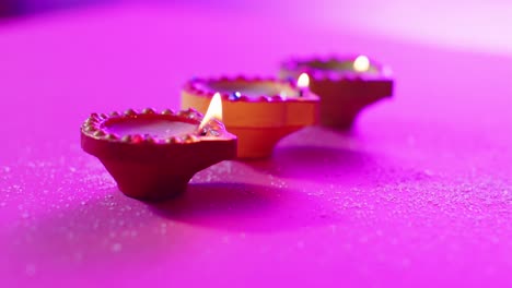 Close-up-of-burning-colourful-candles-celebrating-diwali-on-purple-background