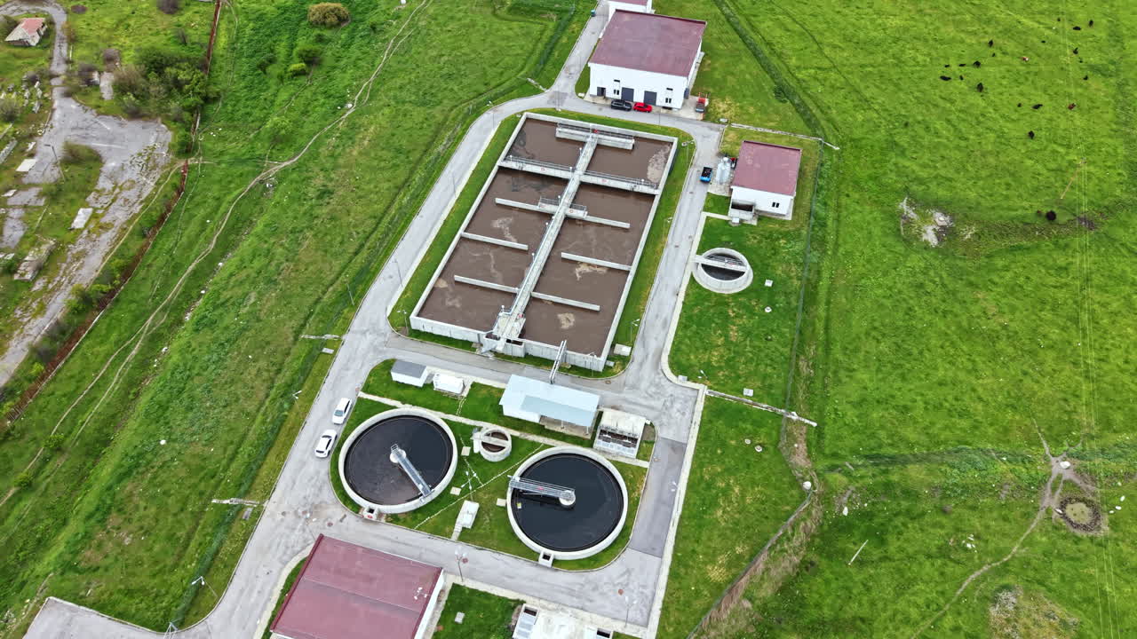 Wastewater treatment facility located in a rural area with green fields and cow pastures nearby showing multiple treatment tanks and office buildings in the daytime